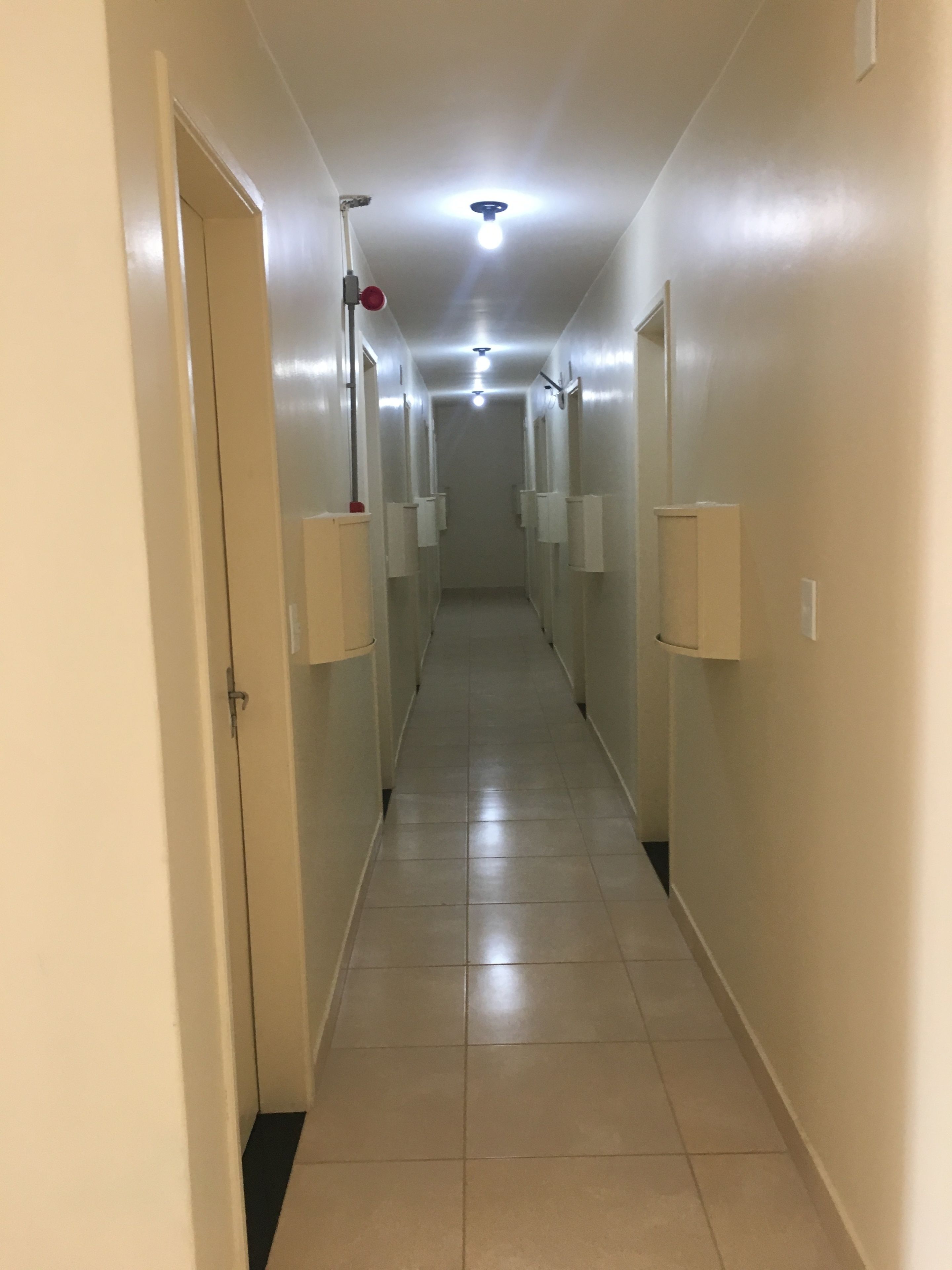 A narrow, well-lit hallway with tiled flooring, white walls, and ceiling lights.