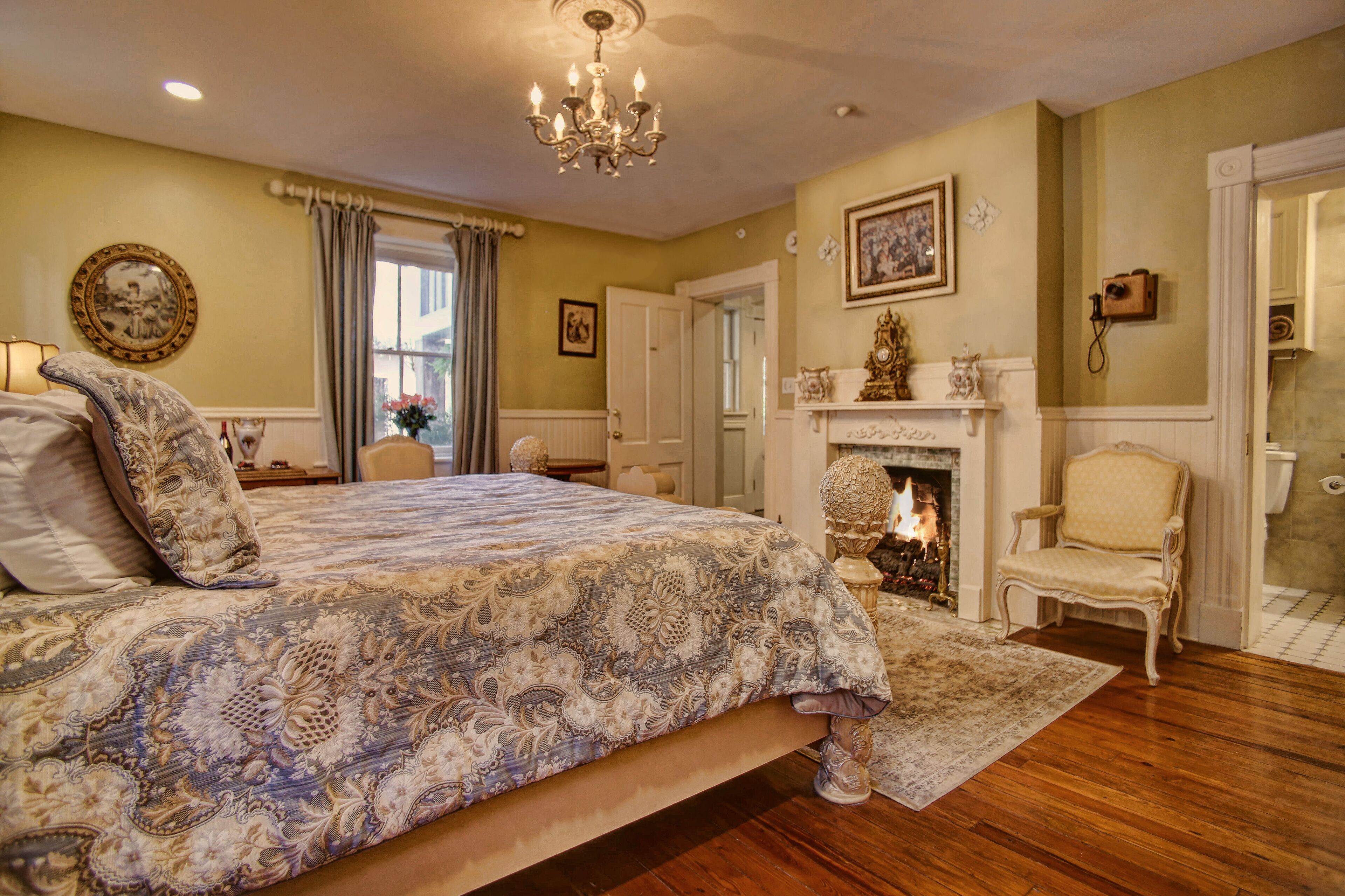 Quarto com uma cama grande, um candelabro, uma lareira e uma cadeira.