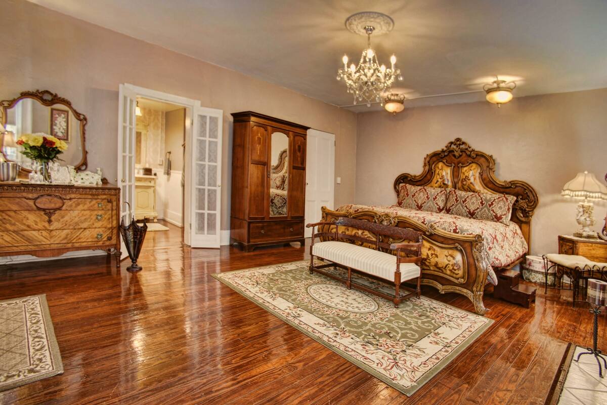 A spacious bedroom with a large bed, a dresser, a vanity, and a chandelier.