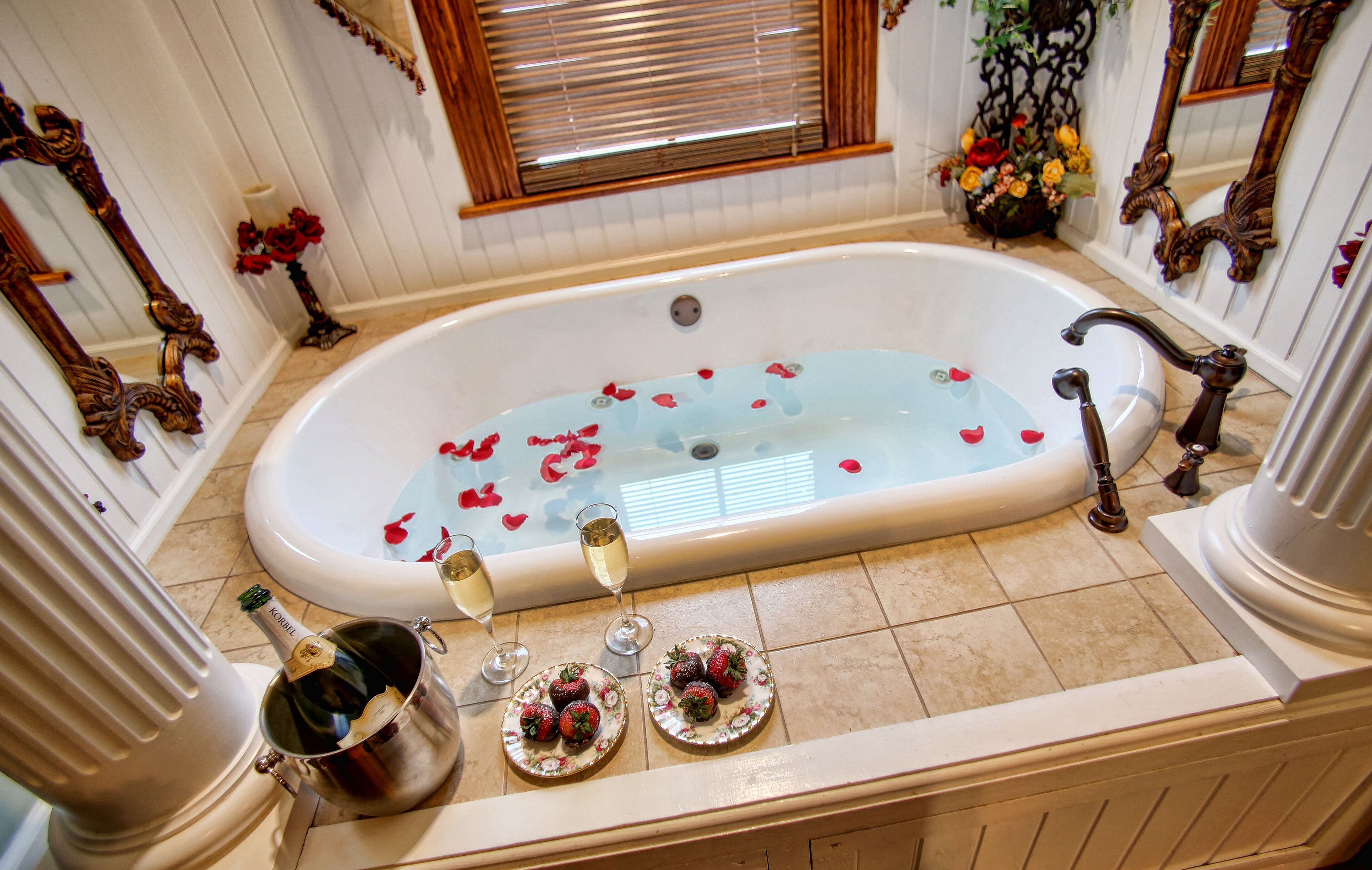 A luxurious bathroom with a bathtub filled with rose petals, champagne, and strawberries.