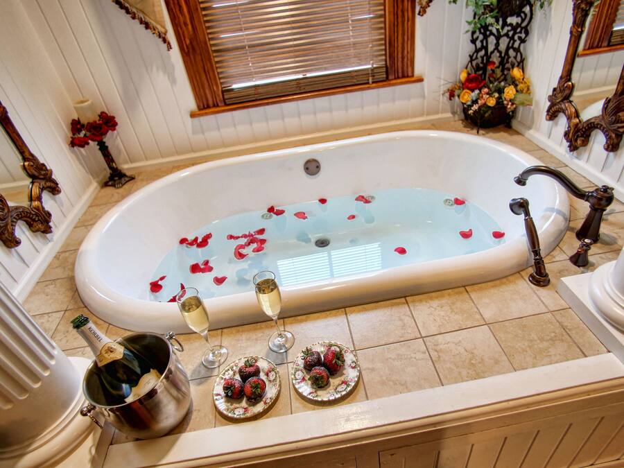 A luxurious bathroom with a bathtub filled with rose petals, champagne, and strawberries.