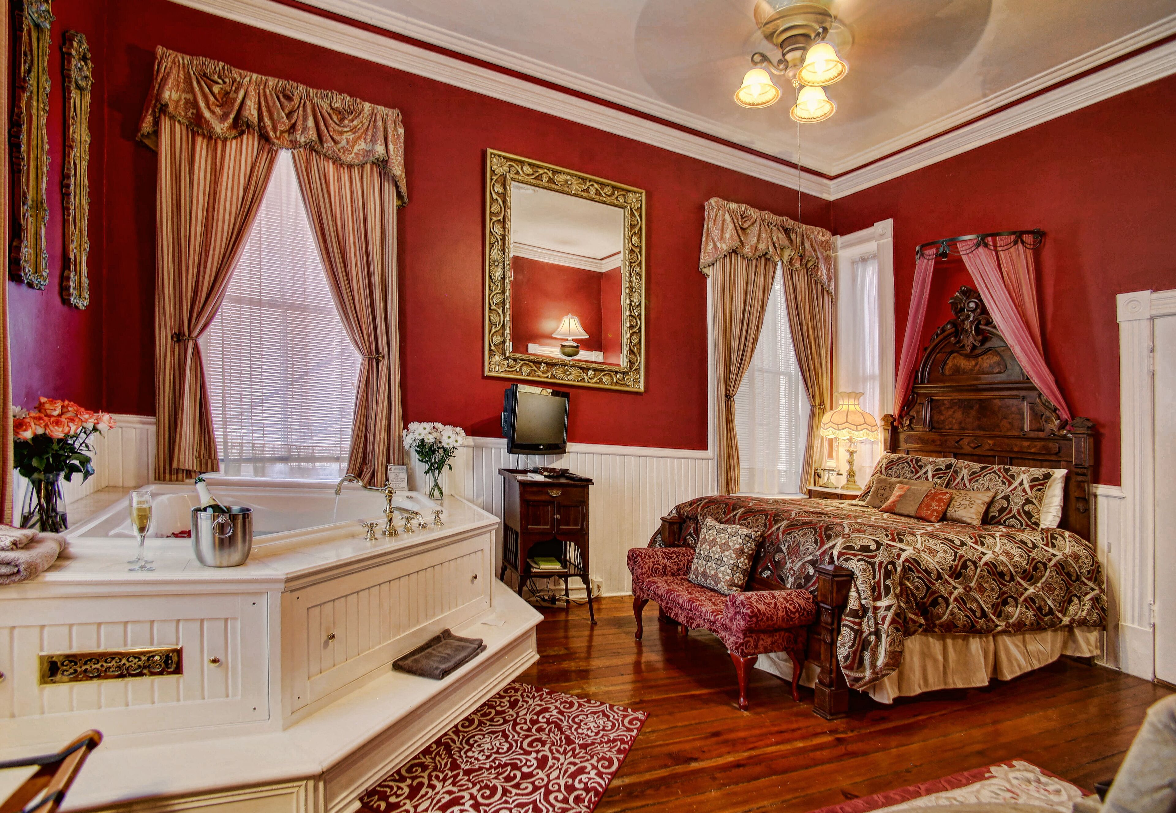 A bedroom with a large bed, a vanity with a mirror, a television, and a red wall.