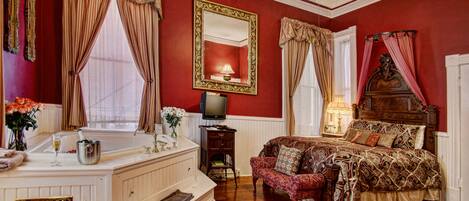 A bedroom with a large bed, a vanity with a mirror, a television, and a red wall.