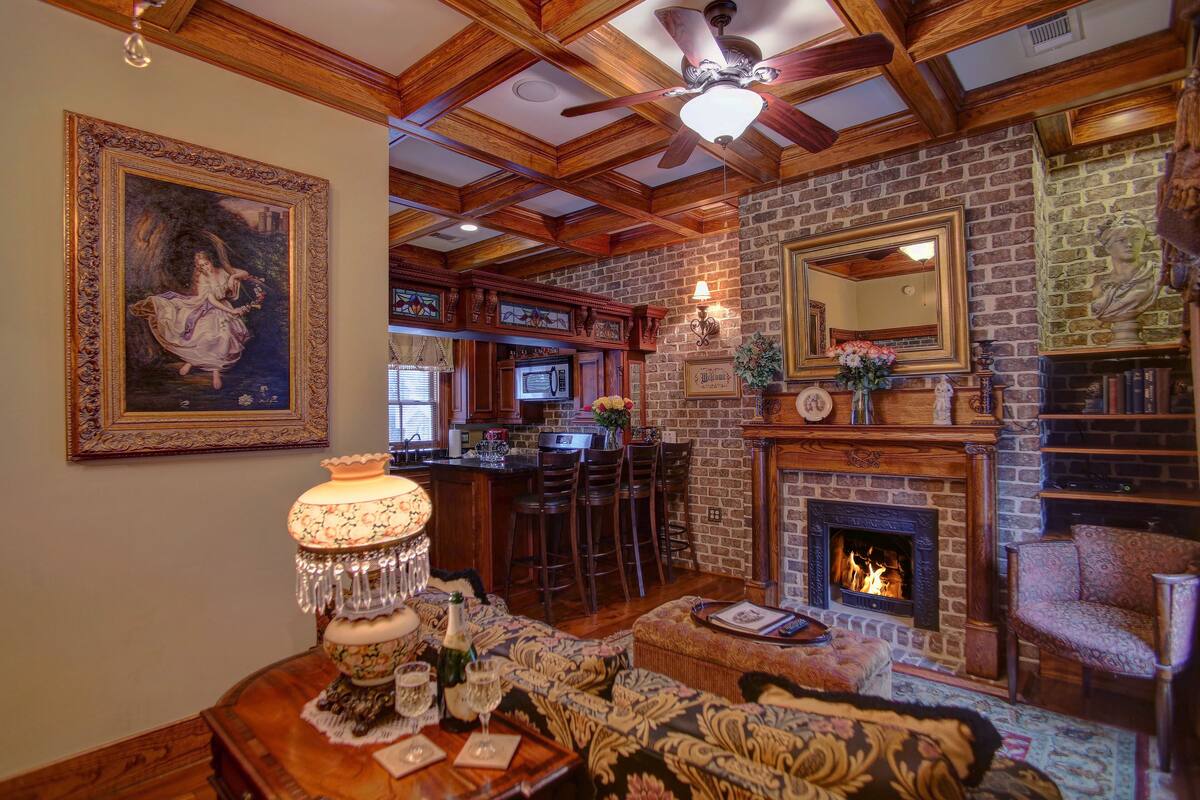 A cozy living room with a fireplace, a dining area with a chandelier, and a kitchen with a bar.