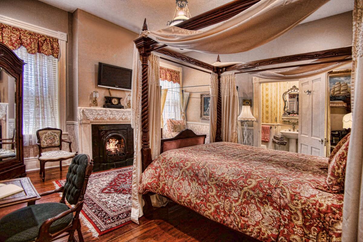A traditional bedroom with a four-poster bed, a fireplace, and classic furnishings.