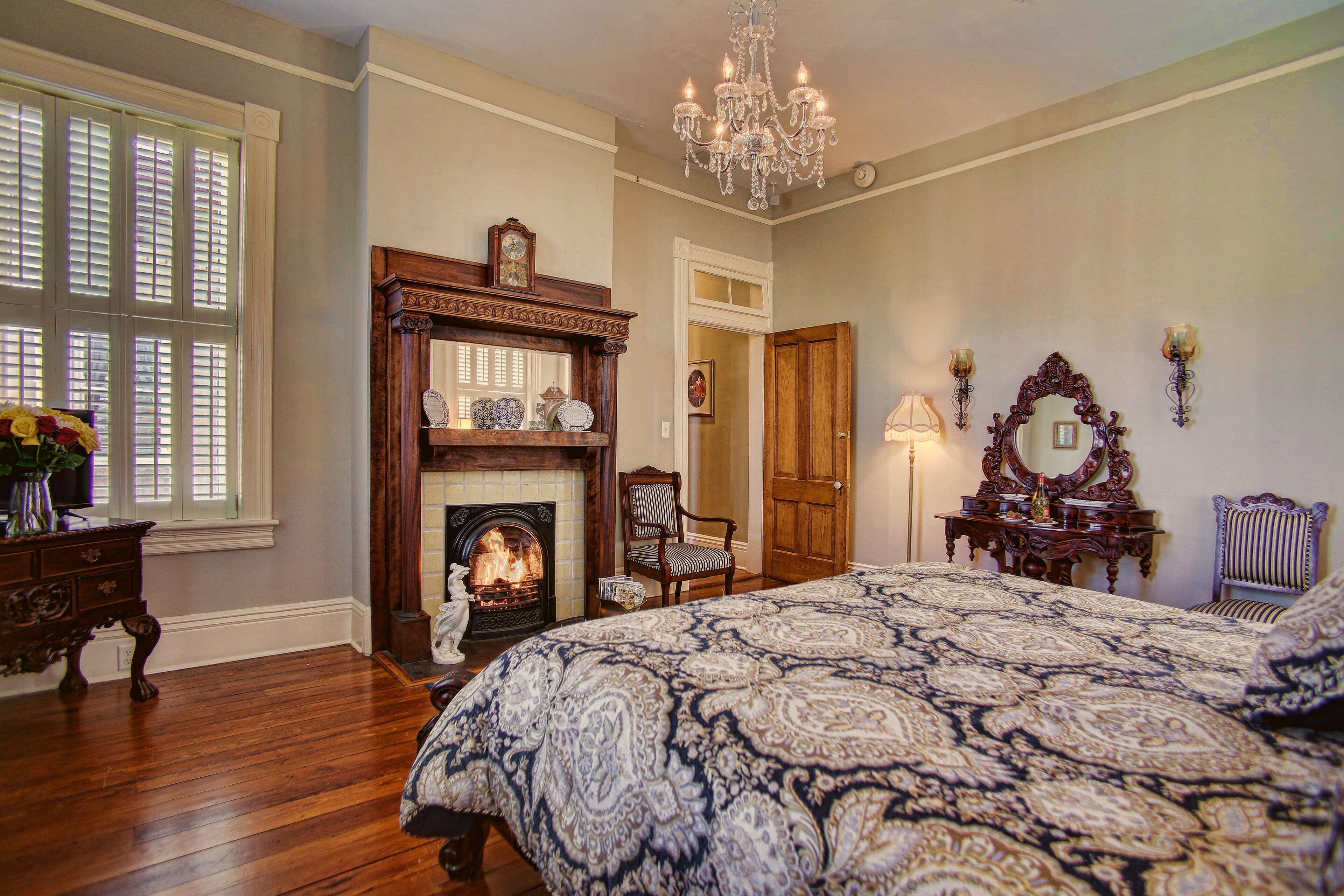 A bedroom with a large bed, a fireplace, a chandelier, and a mirror.