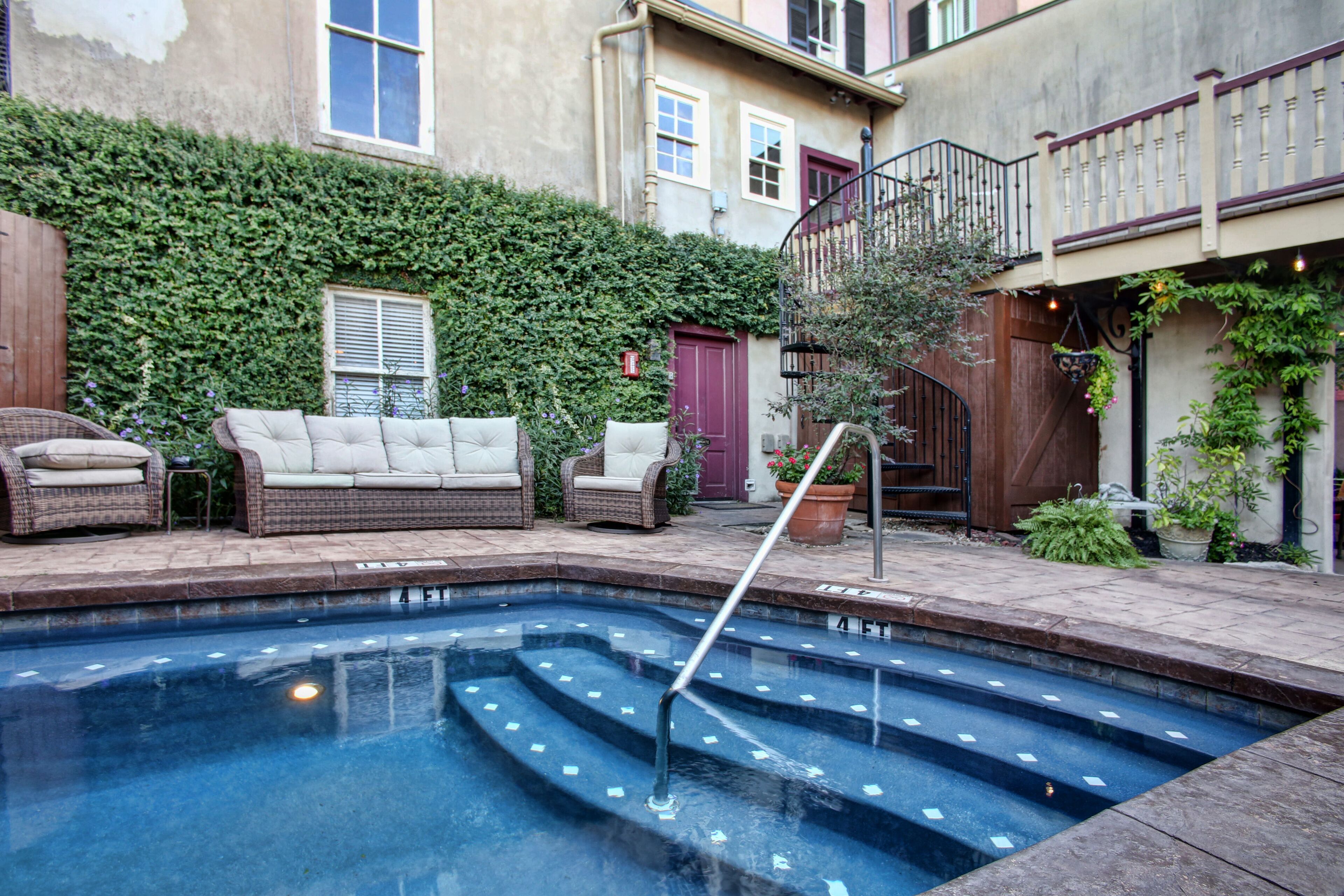 A swimming pool with steps, surrounded by wicker furniture and potted plants.