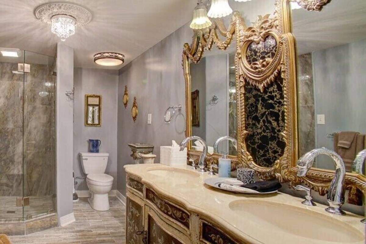 A bathroom with a glass-enclosed shower, a white toilet, and a large ornate mirror.