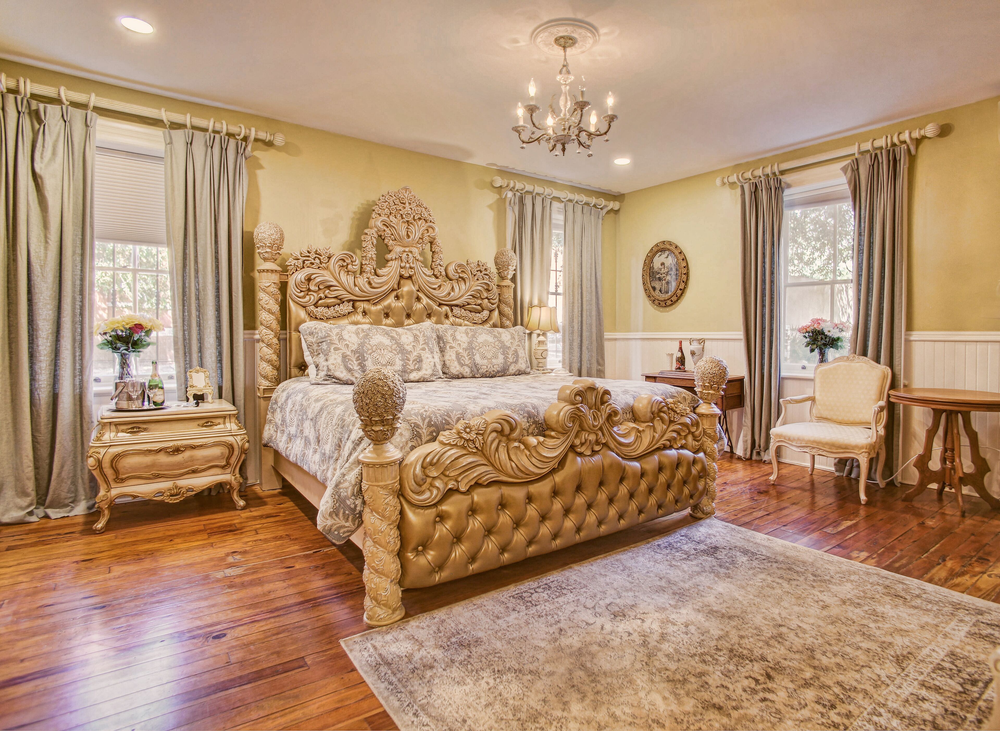 A spacious bedroom with a large ornate bed, a wooden nightstand, a chair, and a small table.