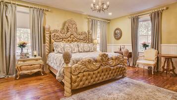 A spacious bedroom with a large ornate bed, a wooden nightstand, a chair, and a small table.