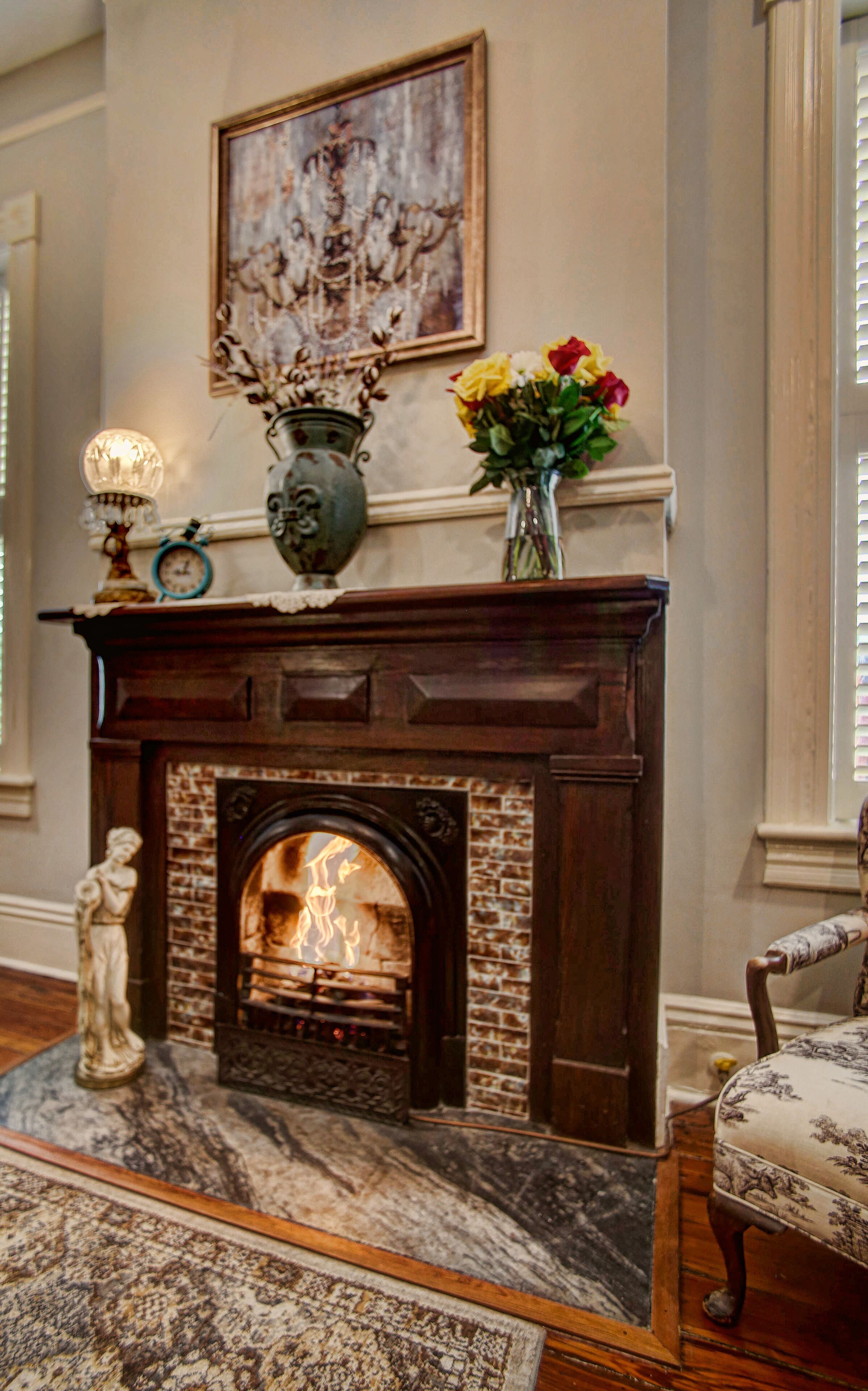 A fireplace with a brick surround, a vase with flowers, and a framed artwork above it.