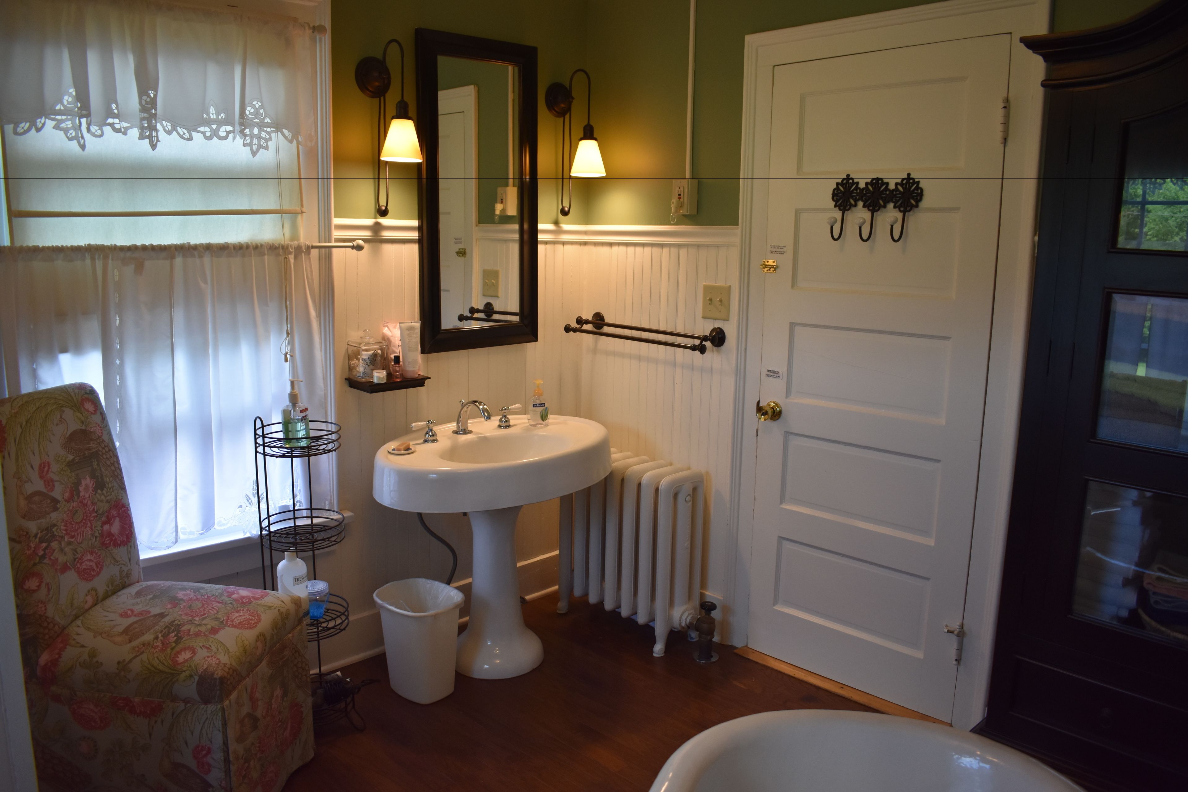 Un baño con un lavabo blanco, un espejo, un radiador, un inodoro y una silla.