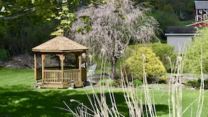 Um gazebo num jardim, com uma casa ao fundo.