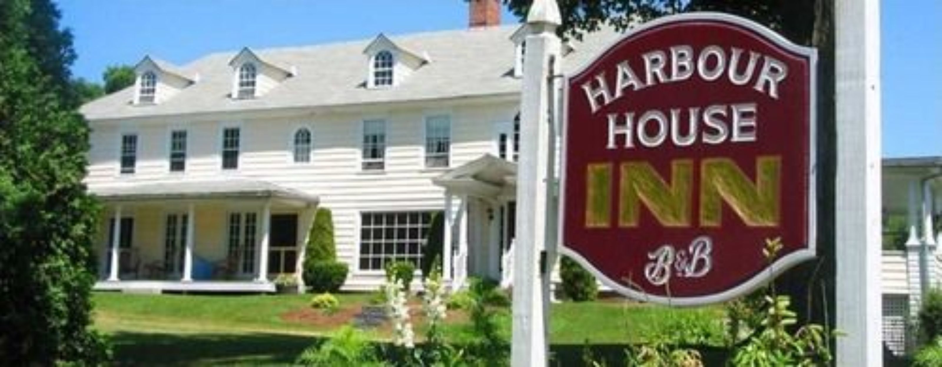 Una casa grande y blanca de dos pisos con un porche y un letrero que dice "Harbour House Inn".