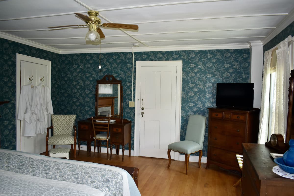 A bedroom with a bed, a dresser, a chair, a desk, a television, and a ceiling fan.