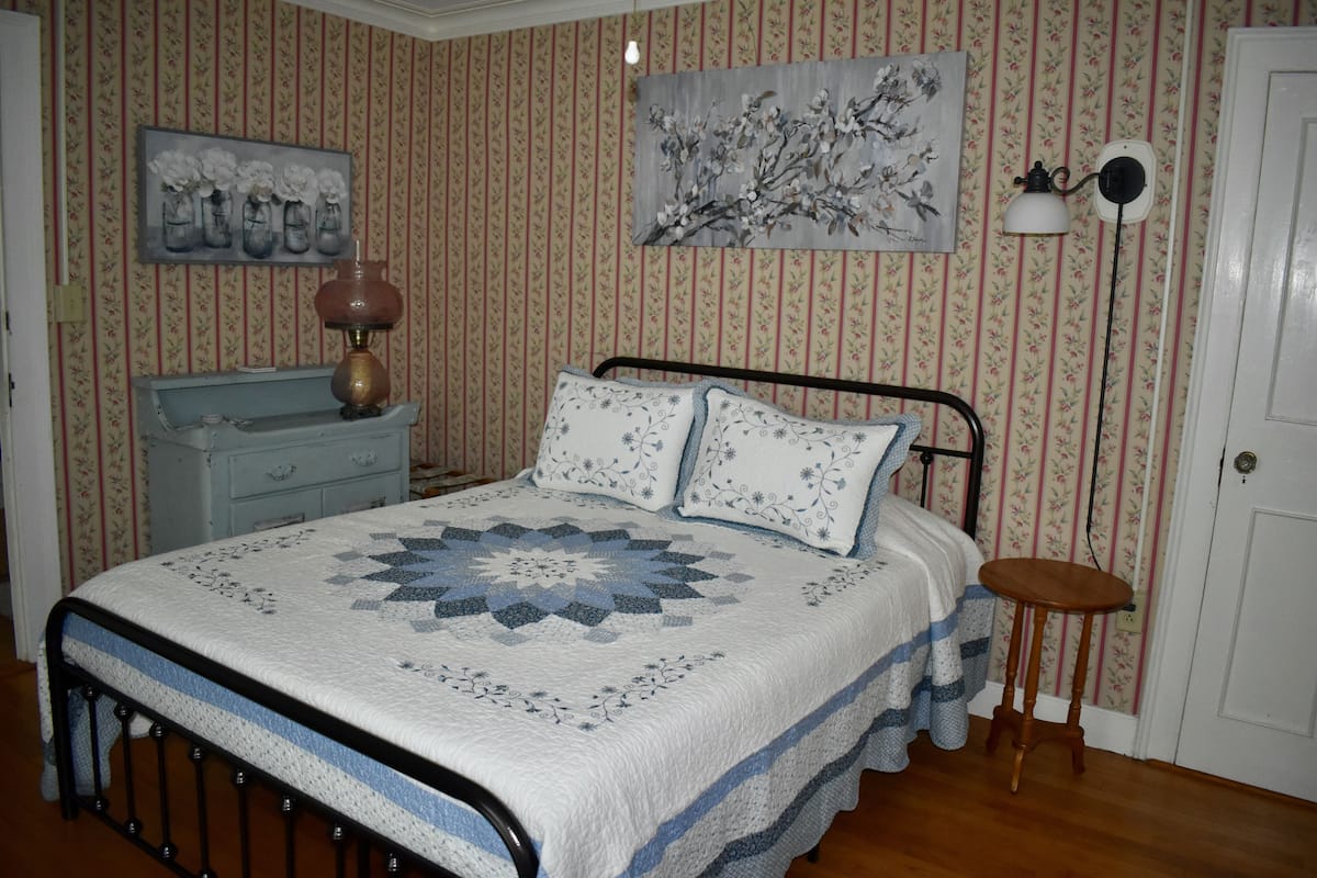 A bedroom with a bed, a dresser, a lamp, and a painting on the wall.