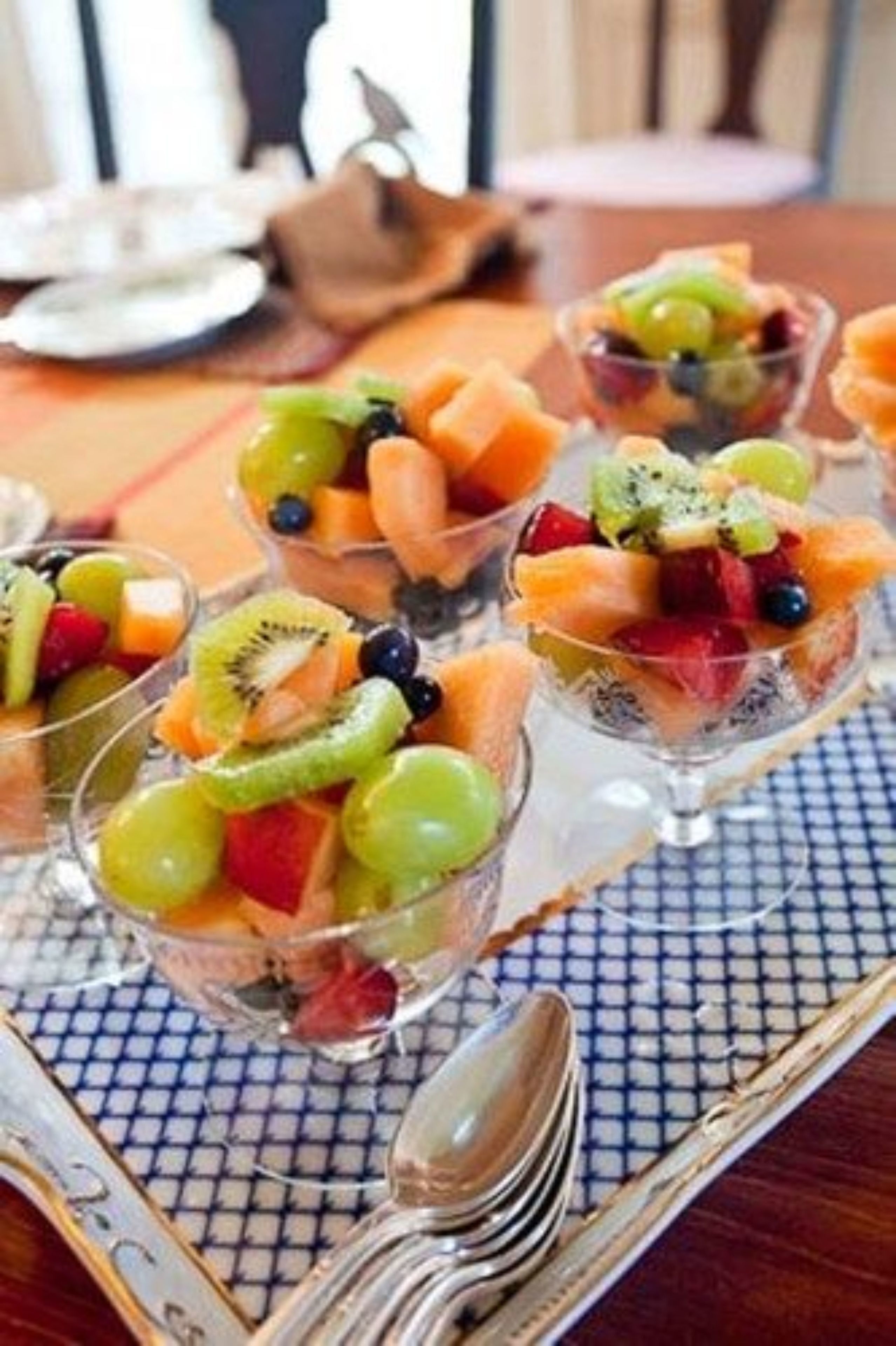 Une table avec des verres en verre transparent contenant une salade de fruits, une cuillère et une serviette.