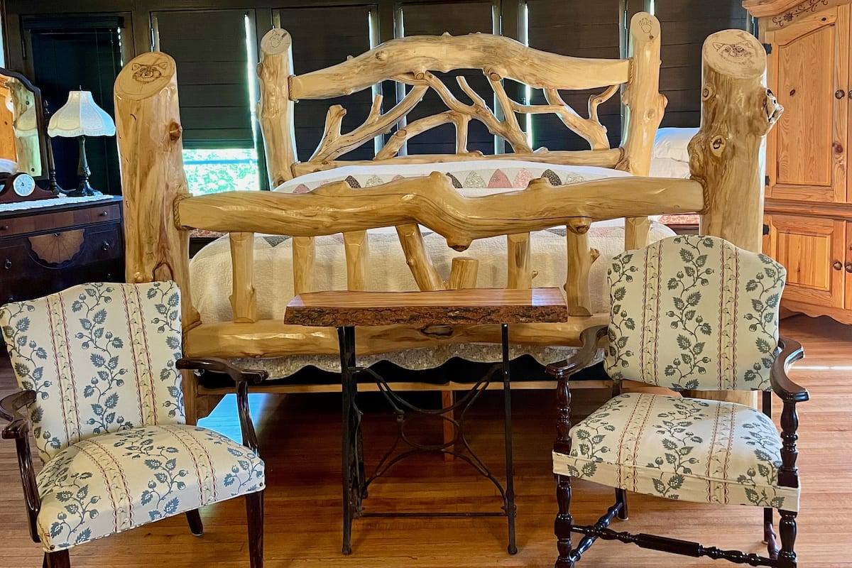A rustic wooden bed with a unique headboard design, flanked by two upholstered chairs with floral patterns.
