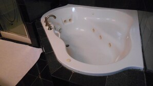 Una bañera blanca independiente con un solo grifo, frente a una pared de azulejos oscuros.