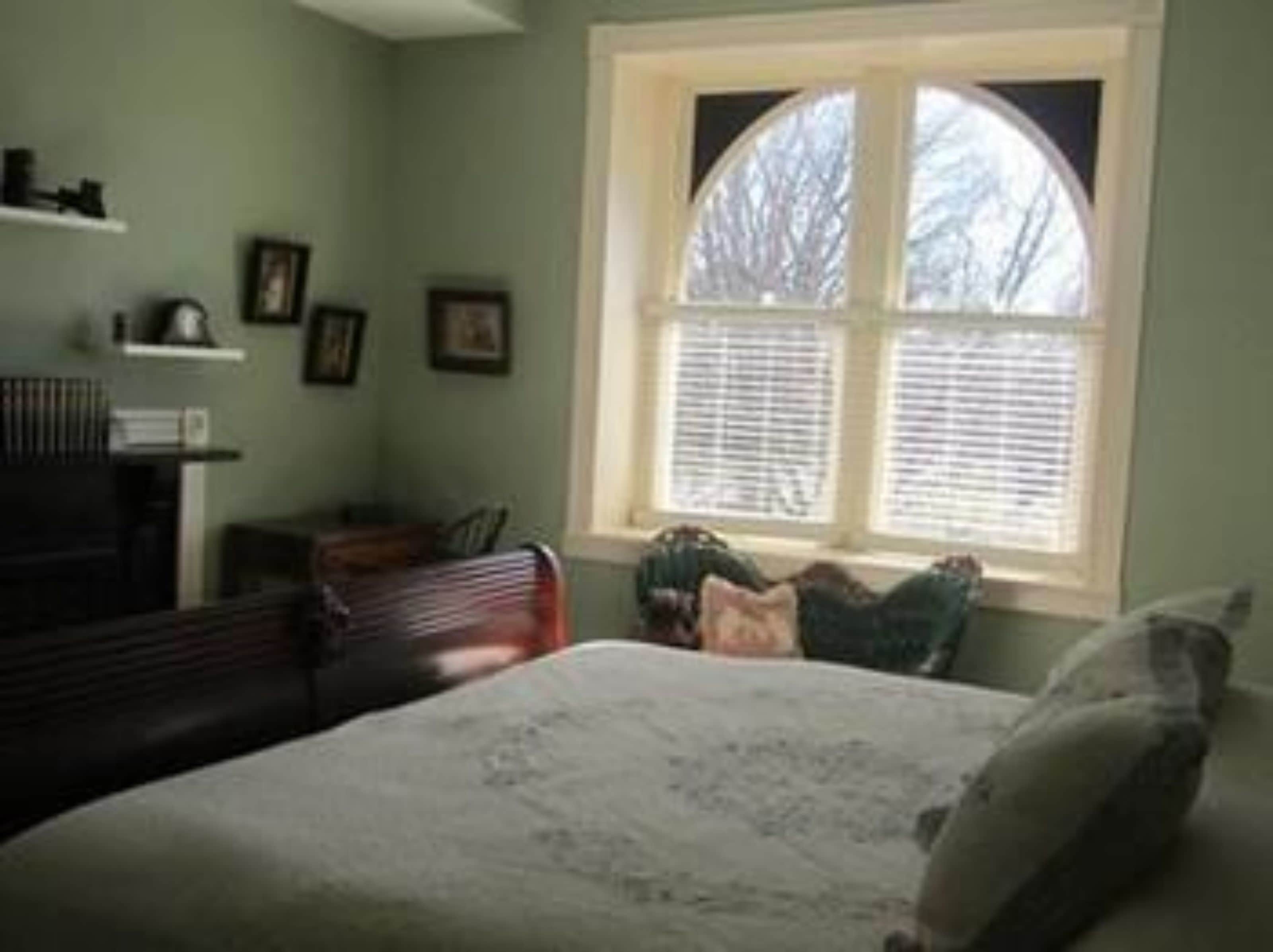 A bedroom with a bed, a window with blinds, a dresser, and a chair.