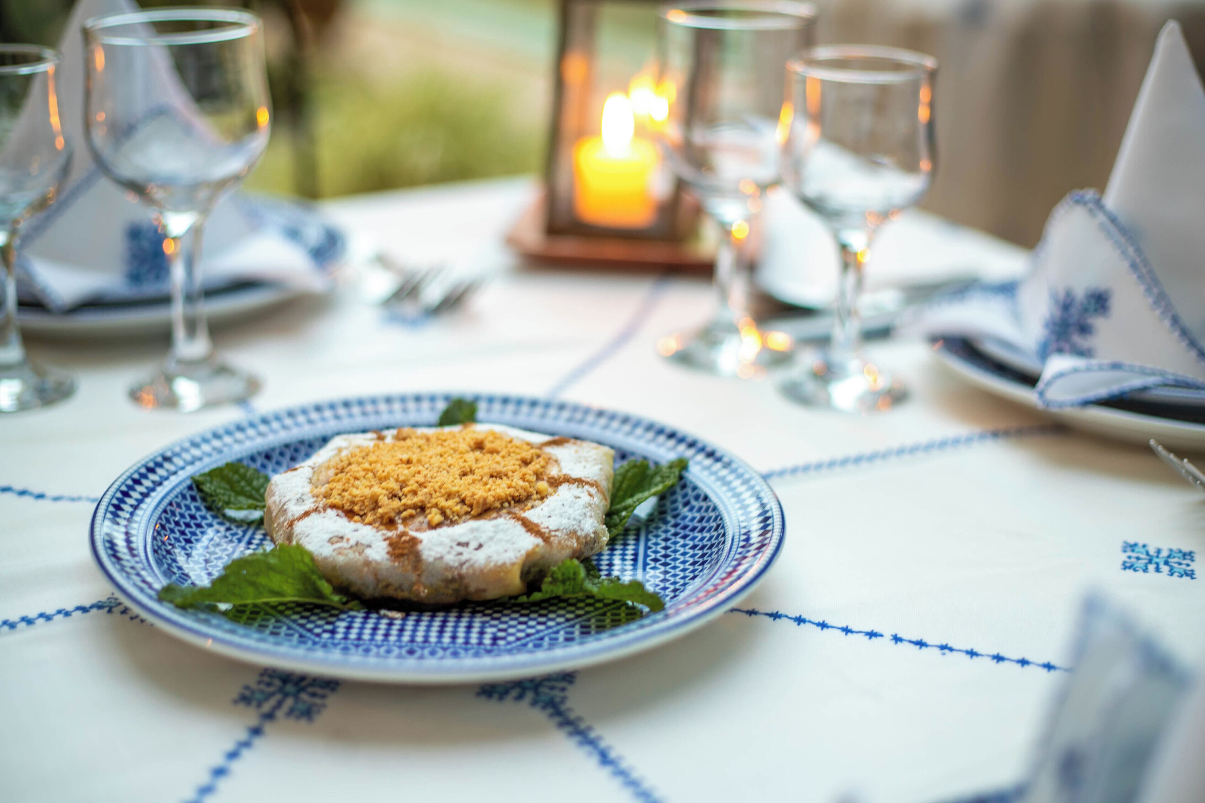 A table set with a plate of food, glasses, and a candle.