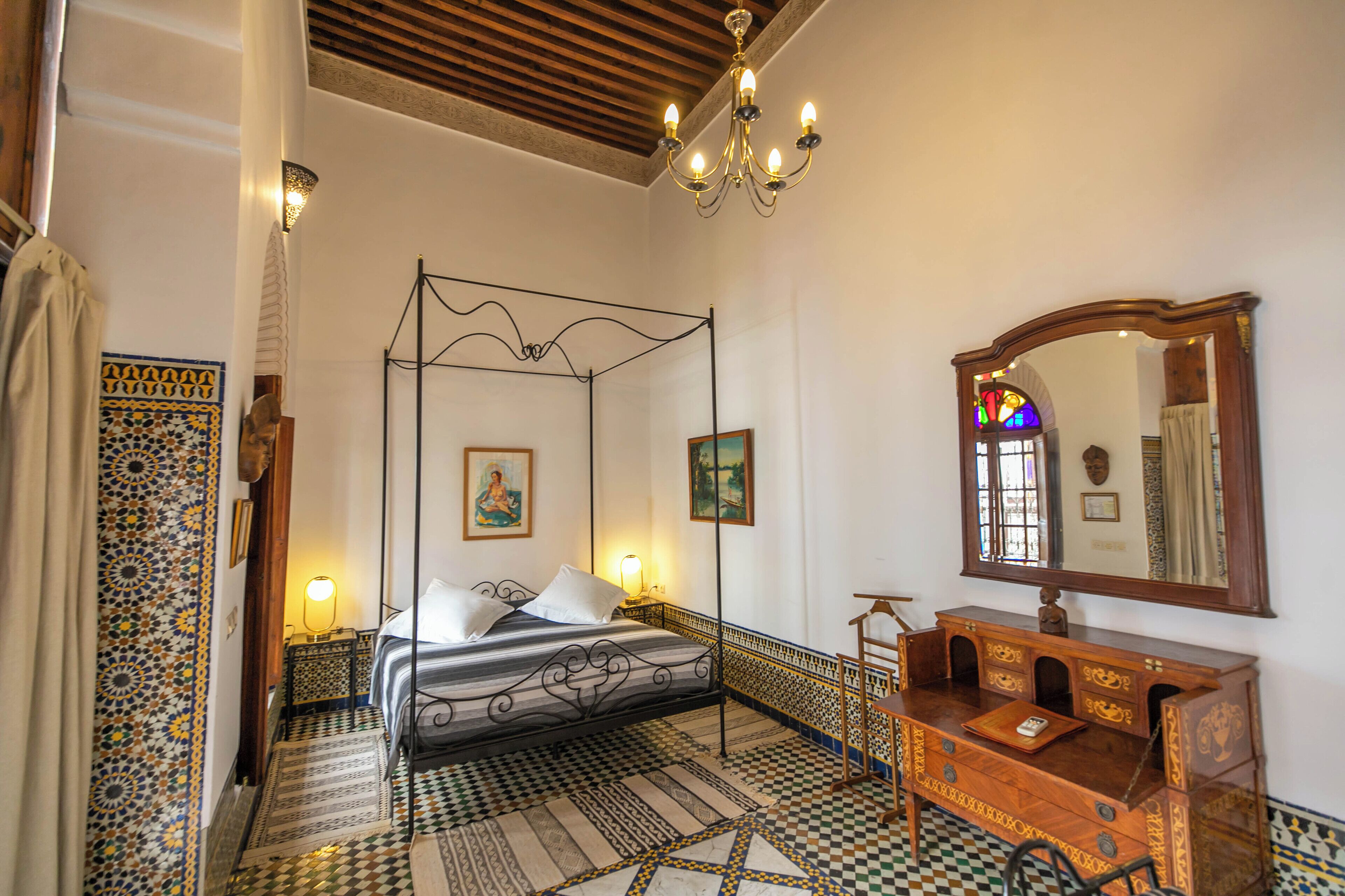 A room with a four-poster bed, a wooden dresser, a mirror, and patterned floor tiles.