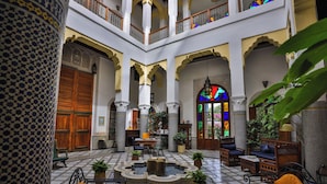 A spacious courtyard with a fountain, seating areas, and a large wooden door.