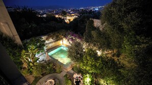 A rooftop garden with a swimming pool, outdoor seating, and a view of the city at night.