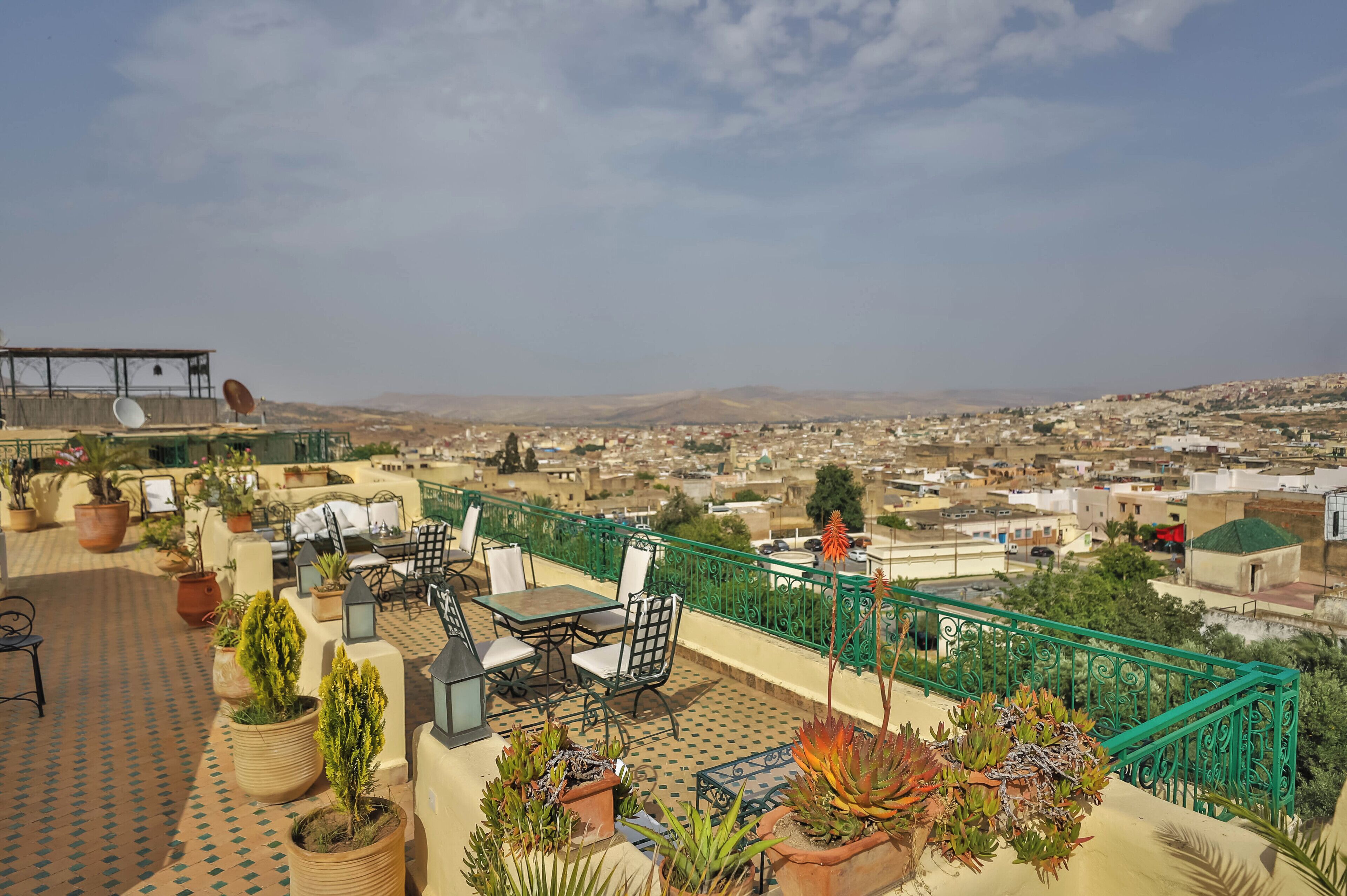 A rooftop terrace with outdoor furniture, potted plants, and a view of a cityscape.
