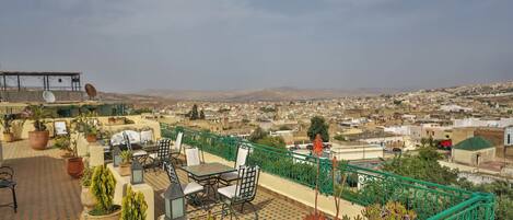A rooftop terrace with outdoor furniture, potted plants, and a view of a cityscape.