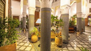 A spacious lobby with high decorative columns, a tiled floor, and potted plants.