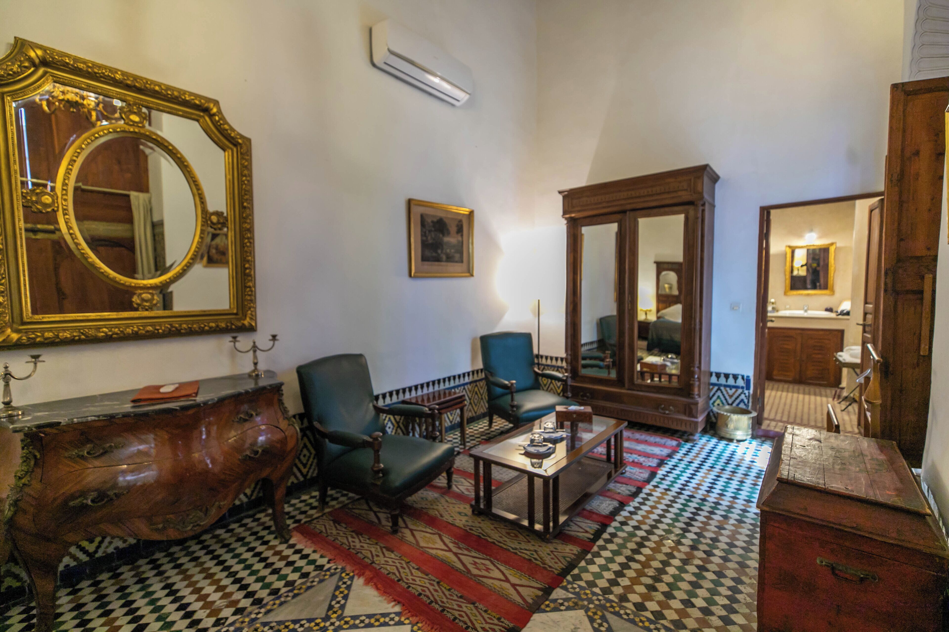 Um quarto com um espelho grande e ornamentado, um armário de madeira, um sofá e um tapete estampado.