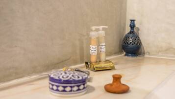 A bathroom shelf with toiletries including a bottle of shampoo, a bottle of shower gel, a small blue vase, and a decorative item.