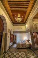 Quarto com cama, lustre e detalhes elaborados nas paredes e no teto.
