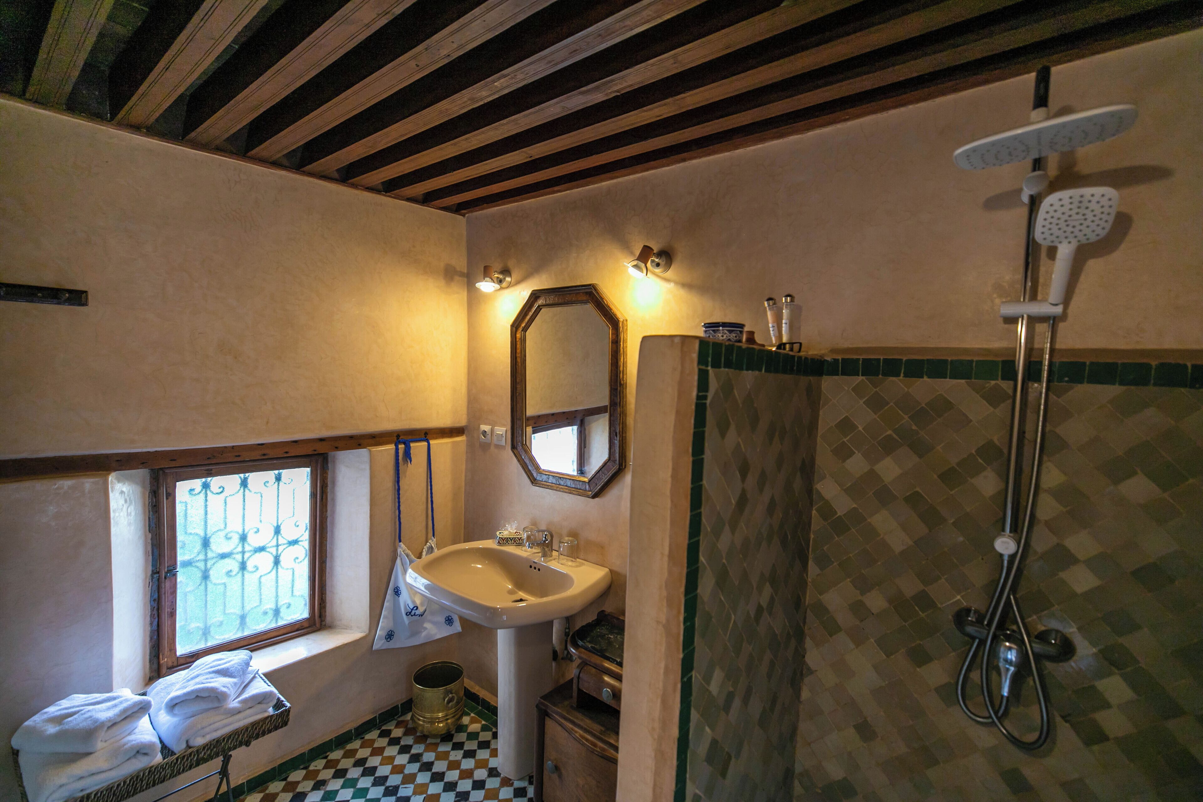 A bathroom with a sink, mirror, shower, and a window with bars.