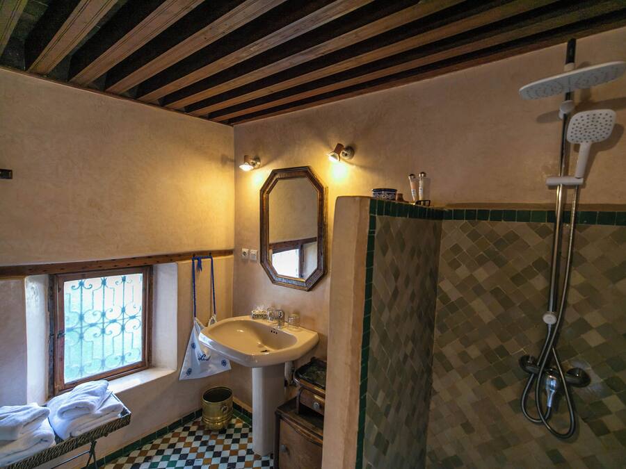 A bathroom with a sink, mirror, shower, and a window with bars.