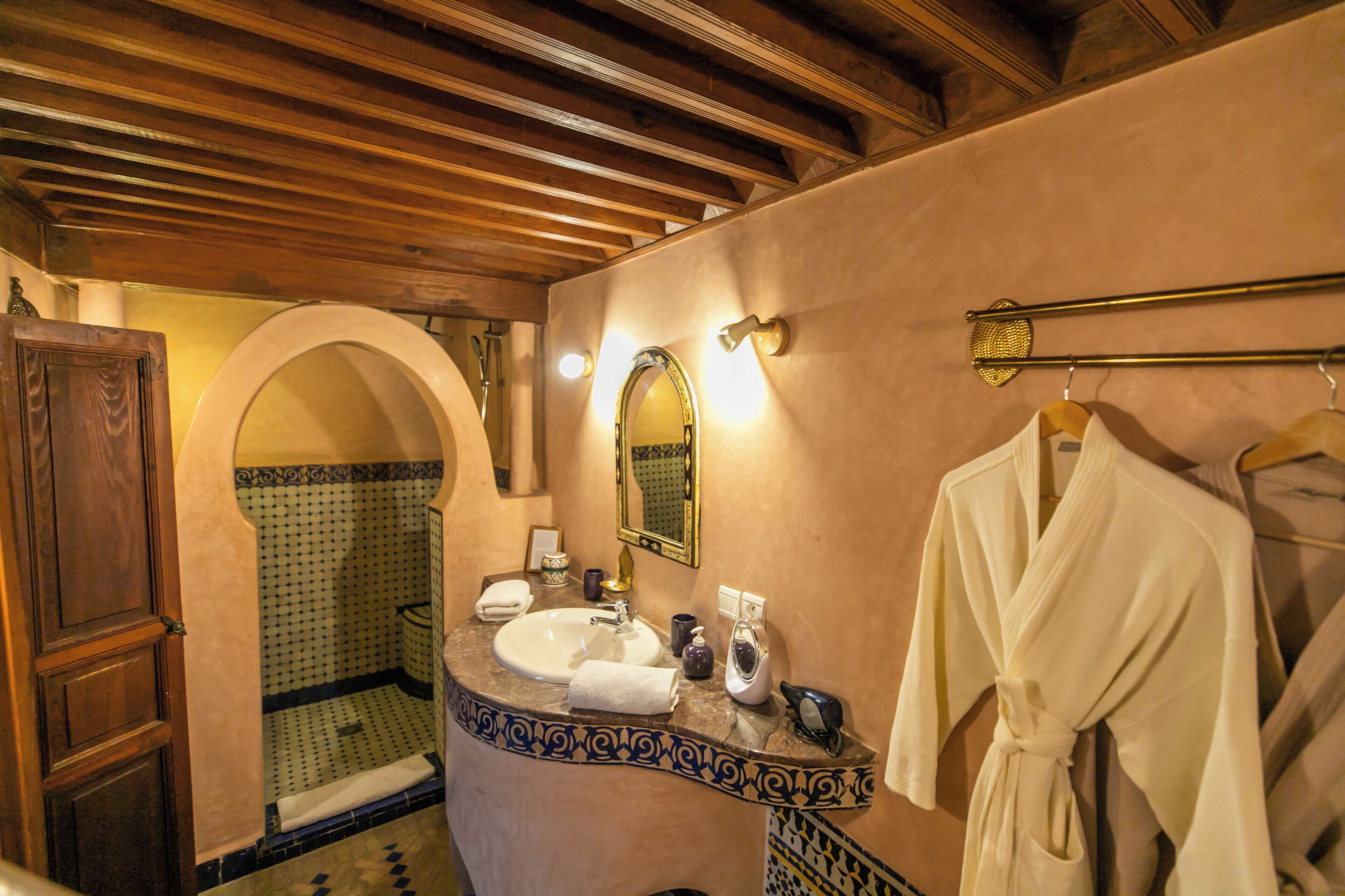 A bathroom with a wooden ceiling, a sink, a mirror, and a robe hanging on a rack.