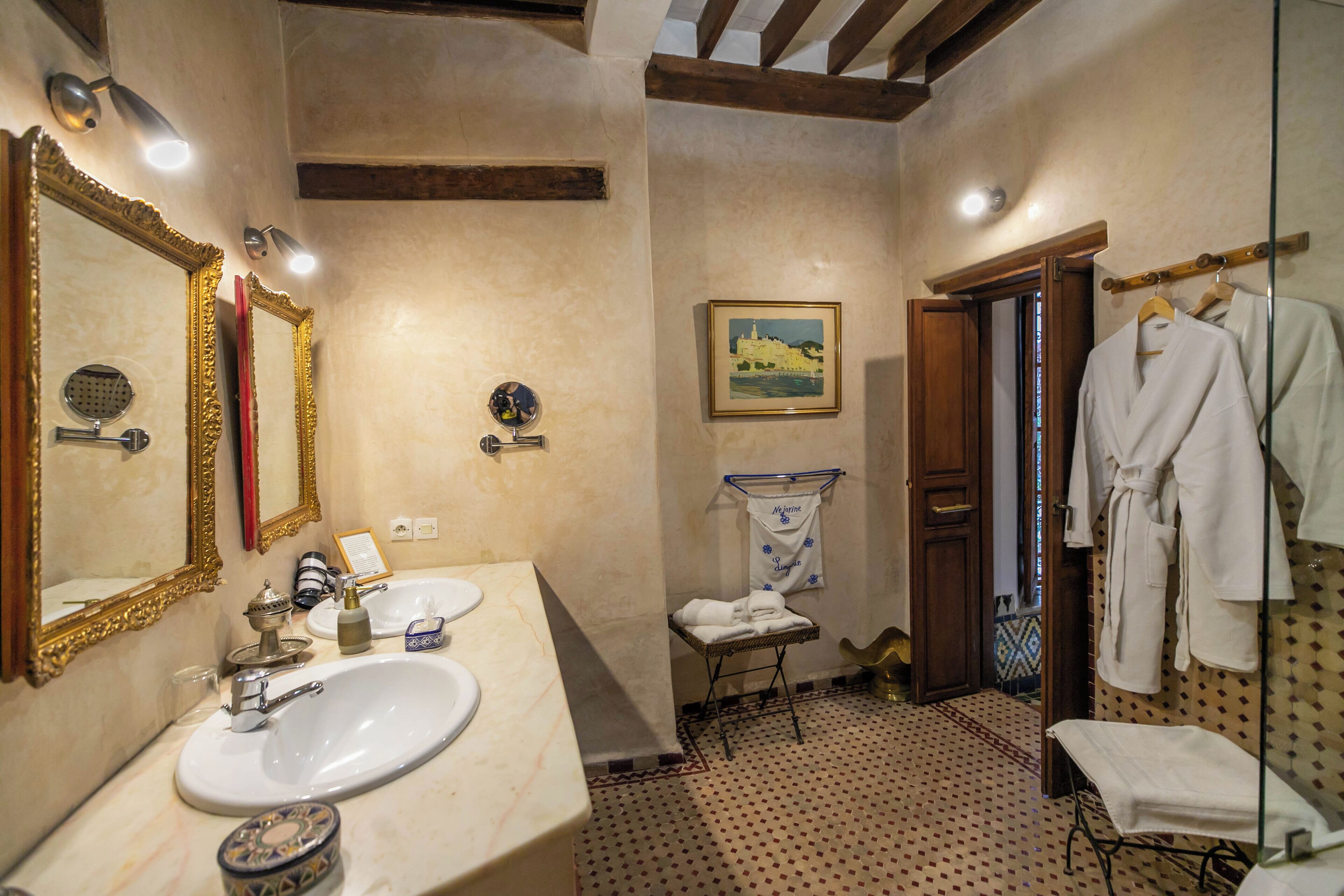 Un baño con dos lavamanos, un espejo grande, un perchero y una puerta que da a otra habitación.