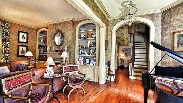 A spacious living room with a grand piano, a fireplace, and a bookshelf. - GardenSong B&B (Natchez)