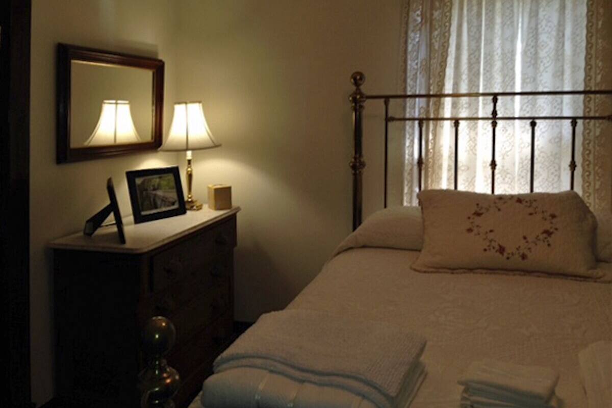 A bedroom with a bed, a dresser, a mirror, and a window with curtains.