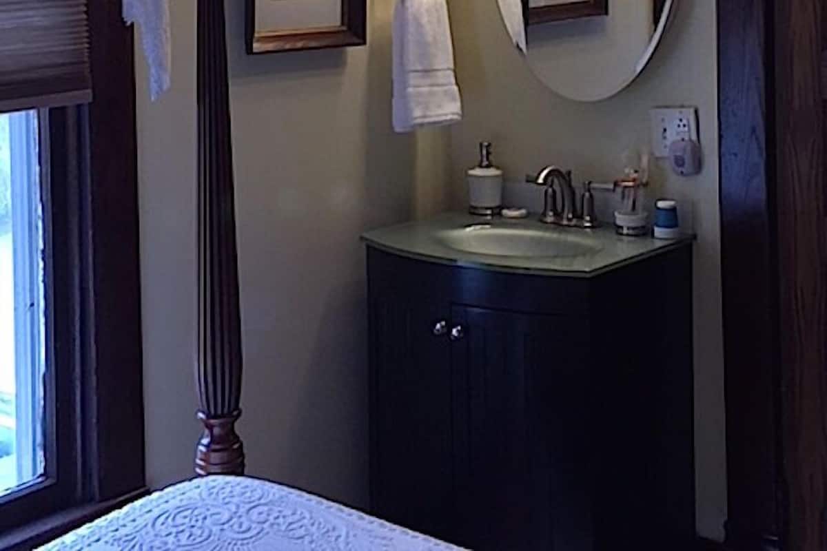 A bathroom with a vanity, a large mirror with lights, a framed picture, and a window with curtains.