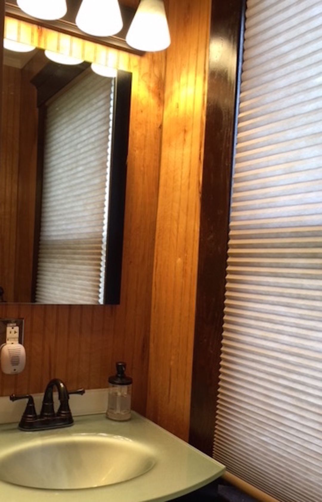 A bathroom with a wooden vanity, a sink, a mirror, and a window with blinds.