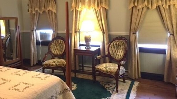 A room with a bed, two chairs, a table with a lamp, and curtains. - River House Lodge (Rowlesburg)