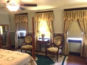 Ein Zimmer mit einem Bett, zwei Sesseln, einem Tisch mit Lampe und Vorhängen.