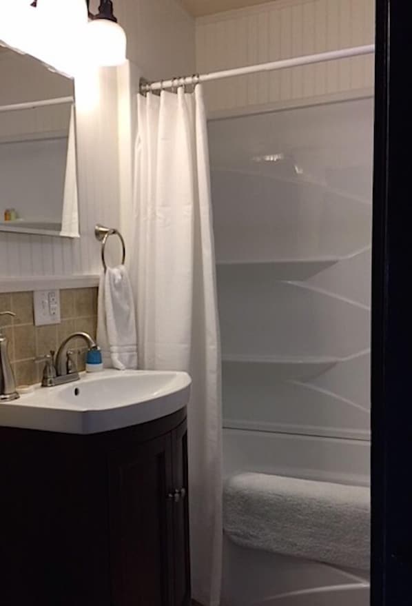 Un baño con lavamanos, espejo, toallero y cortina de ducha.