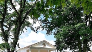 A white building with a central entrance and columns, surrounded by trees. - River House Lodge (Rowlesburg)