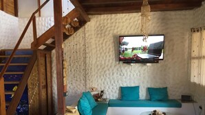 Ein gemütliches Wohnzimmer mit einer Holztreppe, einem türkisfarbenen Sofa, einem an der Wand montierten Fernseher und einem kleinen Tisch mit Dekoration.