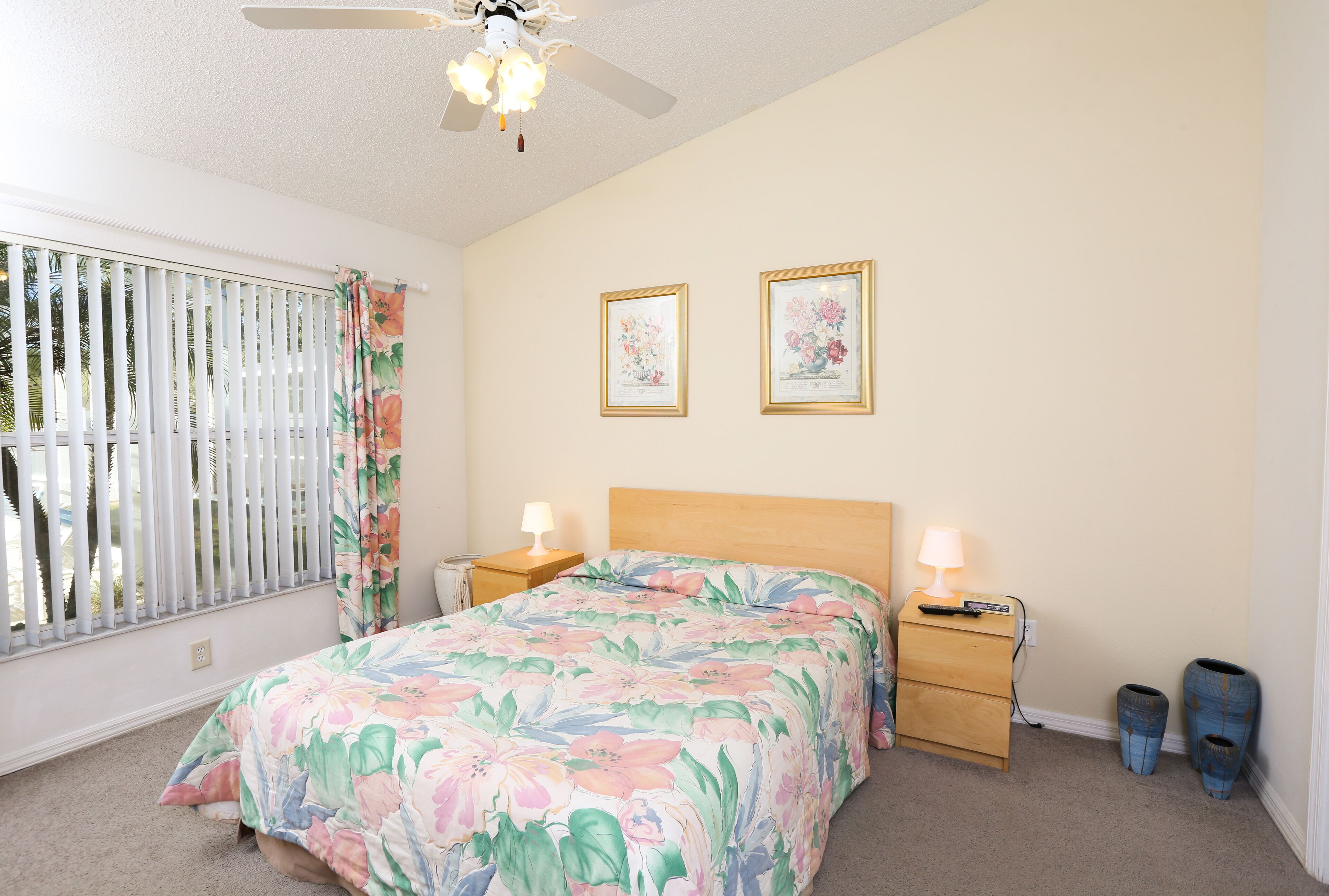 A bedroom with a bed, two bedside tables, a ceiling fan, and a window with blinds.