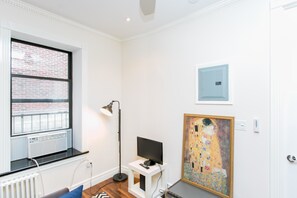Ein Zimmer mit Heizkörper, einer schwarzen Stehlampe, einem Fernseher auf einem weißen Schrank und einem großen Gemälde an der Wand.