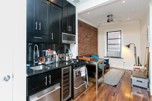 A modern kitchen with black cabinets, stainless steel appliances, and a brick accent wall. - NY056 1 Bedroom Apartment By Senstay (Elizabeth)